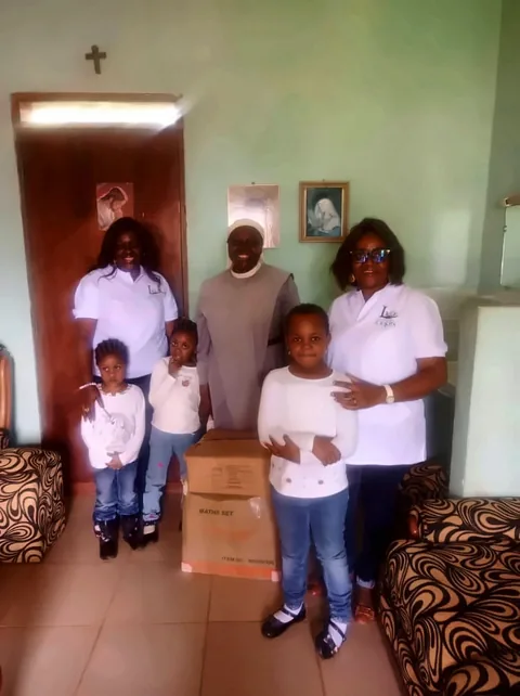 Photo de groupe au monastère : membres de la fondation, la sœur et des enfants, autour des cartons de fournitures
